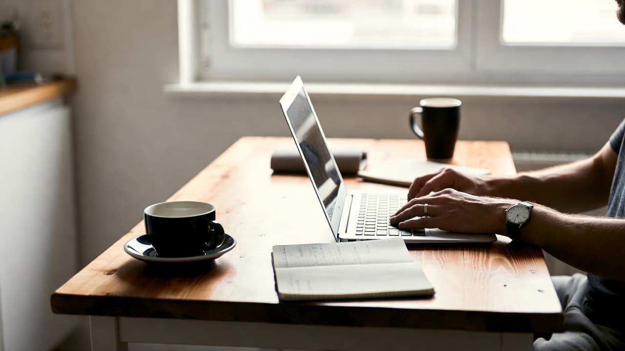 Freelancer am Küchentisch mit Laptop und Notizbuch bei Tageslicht