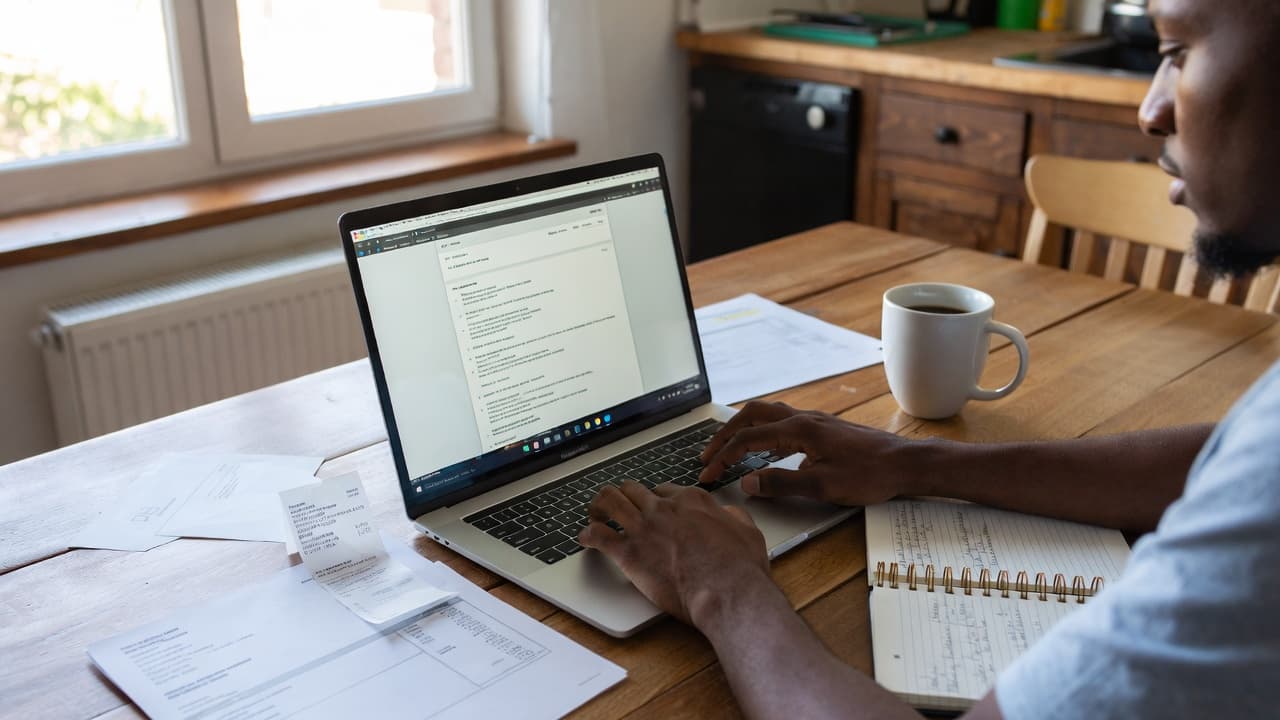 Freelancer am Küchentisch mit Laptop und Rechnungen