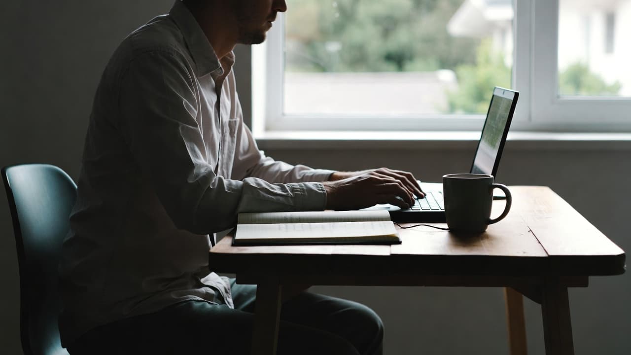 Freelancer am Schreibtisch mit Notizbuch und Laptop bei natürlichem Licht